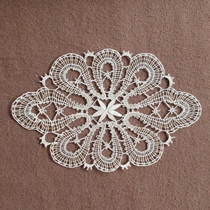 May include: A delicate white lace doily with a floral design. The doily is made of fine thread and has a delicate, intricate pattern.