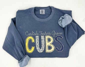 May include: A blue sweatshirt with the text "Carlisle Foster's Grove CUBS" in yellow, white, and blue patterned letters.