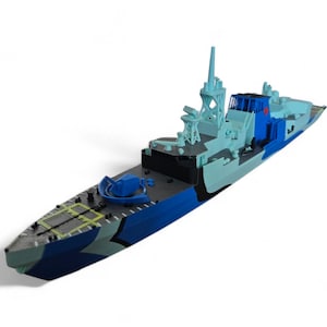 Peut inclure: Maquette de navire de guerre aux tons de bleu, gris et noir. Le jouet présente un design détaillé avec des tourelles, une passerelle et d'autres éléments militaires. Le navire est sur fond blanc.