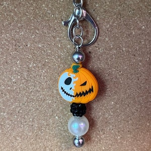 May include: A silver keychain with a pumpkin charm. The pumpkin is split in half, one side is white with a Jack Skellington face, the other side is orange with a traditional pumpkin face.