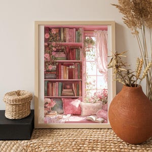 May include: A framed print depicting a cozy reading nook with a pink bookshelf filled with books. The scene includes pink pillows, a window with pink curtains, and floral accents. A woven basket and a terracotta vase are in the foreground.