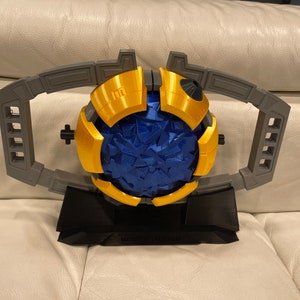May include: A 3D printed model of a blue and gold sphere with a textured surface, mounted on a black stand. The sphere is surrounded by a gray, 3D printed frame with a handle.
