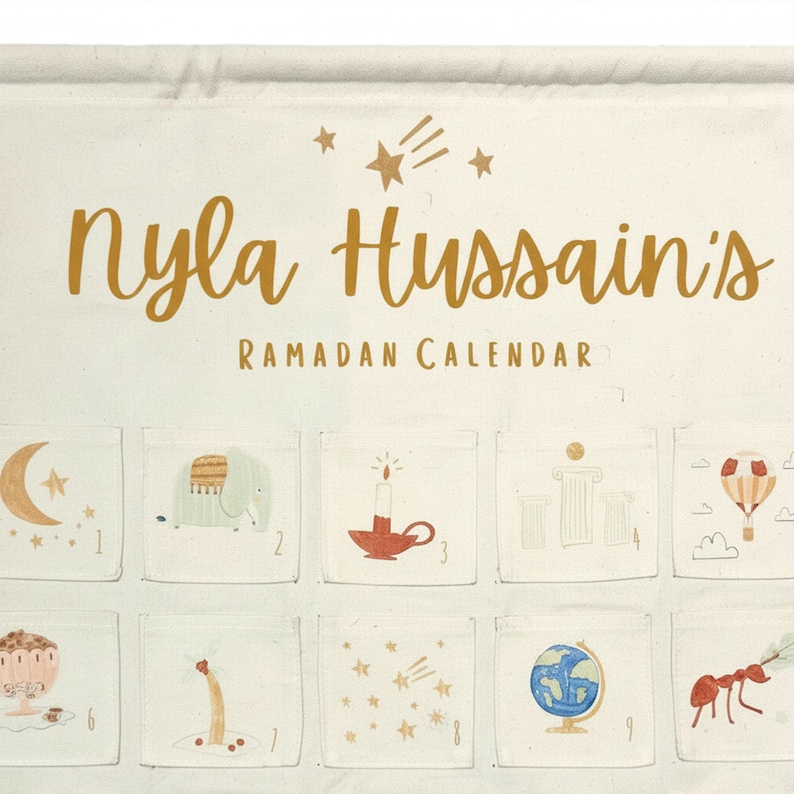 May include: Ramadan calendar with the text "Nyla Hussain's Ramadan Calendar" in gold script. The calendar has small pockets with illustrations of a crescent moon, elephant, candle, and other festive images.