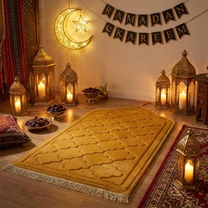 Puede incluir: Una escena cálida de Ramadán con una alfombra de oración amarilla con un diseño estampado, rodeada de linternas encendidas y cuencos de dátiles. Una lámpara de luna creciente y estrella cuelga arriba, con una pancarta que dice "Ramadán Kareem".