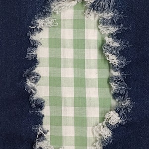 May include: A close-up of a ripped denim fabric with a green and white gingham patch sewn in the hole.