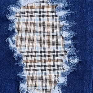 May include: A close-up of a blue denim fabric with a distressed hole revealing a brown and white plaid fabric underneath.