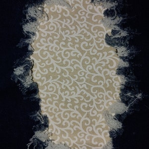 Peut inclure: Gros plan sur un tissu en jean délavé avec un trou révélant un tissu beige à motif floral blanc.