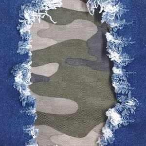 May include: A close-up of a pair of blue denim jeans with a ripped hole revealing a camouflage fabric underneath.