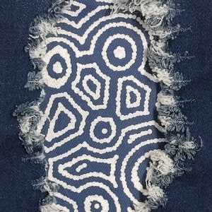 May include: A close-up of a blue denim fabric with a white geometric pattern in a hole. The hole is frayed and has a distressed look.