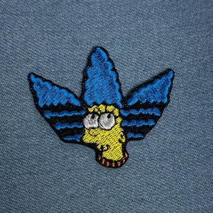 May include: Embroidered patch featuring a cartoon character with blue hair and a yellow face. The patch has black and blue accents and is set against a blue denim background. The design is a stylized representation of a well-known animated character.