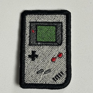 Peut inclure: Écusson brodé représentant une console de jeu portable rétro. Le patch a un fond gris avec une bordure noire. L'écran est vert et les boutons sont noirs et rouges. Un accessoire nostalgique pour les joueurs.