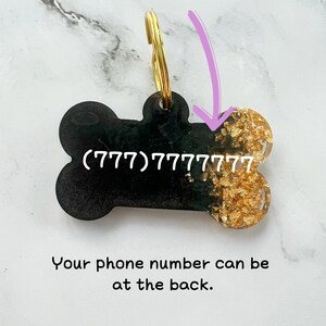 Op de afbeelding: Zwarte, botvormige hondenhanger met een gouden glitteraccent. De hanger heeft een gouden ring en het telefoonnummer (777) 777 7777 staat erop gedrukt.