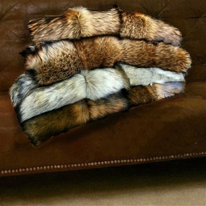May include: A stack of four faux fur throws in shades of brown, grey, and white. The throws are arranged on a brown suede sofa.