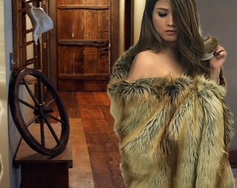 May include: A woman wearing a brown and black faux fur shawl. The shawl is draped over her shoulders and she is holding a strand of the fur in her hand. The woman is standing in a hallway with a wooden door and a wooden wheel on a table in the background.