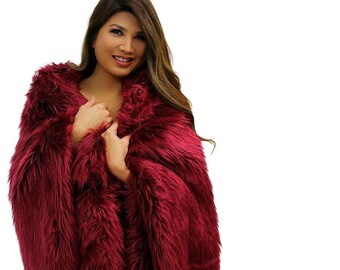 May include: A woman wearing a long, burgundy faux fur coat. The coat is soft and fluffy, and the woman is smiling.