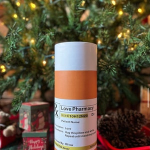 May include: Orange and white pill bottle with a label that reads "Love Pharmacy" and "RX#:C10H12N20". The label also includes the words "Patient Name", "Description: Love", "Directions: Hug this pillow and smile. Repeat until mood improves", "Distributed By: Pill-ow", and "Expiration: Never".