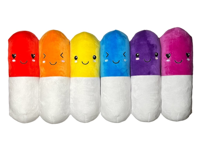 May include: Seven plush pill-shaped toys in a rainbow of colors, each with a different happy face. The pills are red, orange, yellow, blue, purple, and pink.
