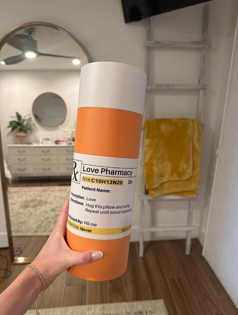 May include: Orange and white pill bottle with the text "Love Pharmacy" and "RX#:C10H12N20 Dr."  The bottle has the text "Prescription: Love" and "Directions: Hug this pillow and smile. Repeat until mood improves."  The bottle also has the text "Distributed By: Pill-ow" and "Expiration: Never".