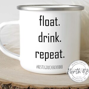 May include: White enamel mug with a silver rim and handle. The mug features the words "float. drink. repeat." in black block letters. Below the text is the hashtag #RESTIGOUCHERIVERNB and a circular logo.