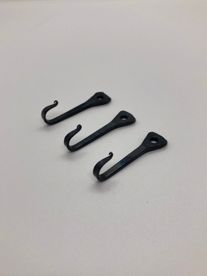 May include: Three black metal hooks with a simple design. Each hook has a pointed end and a curved hook.