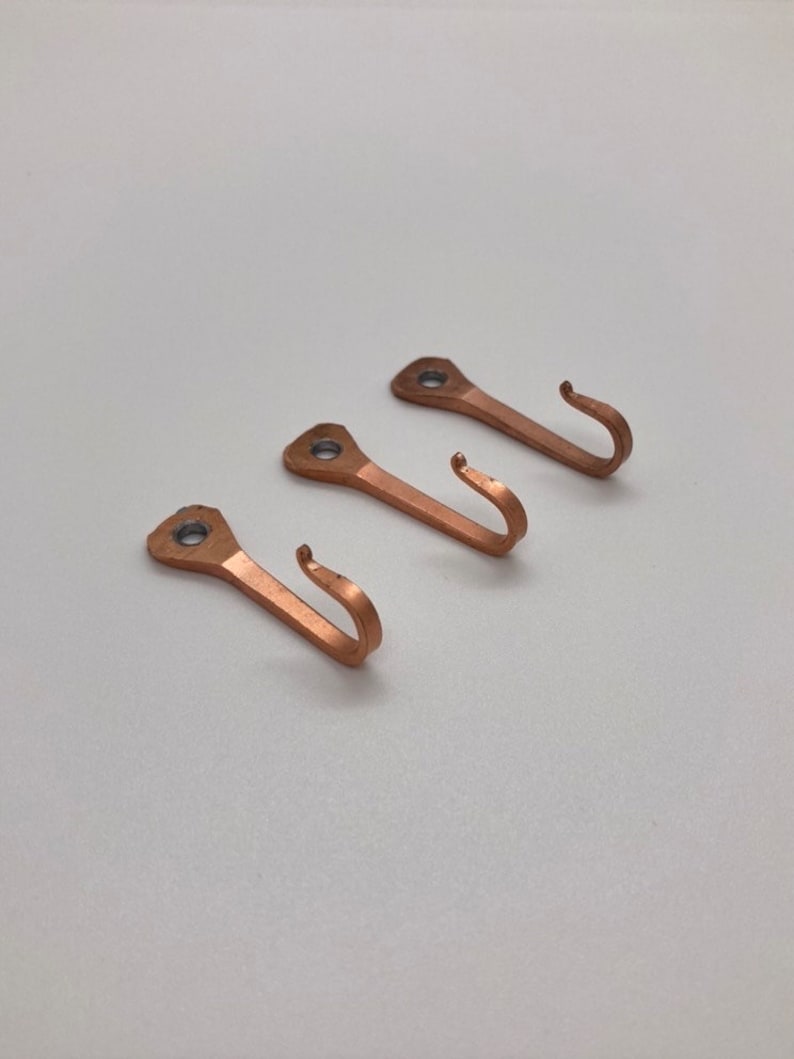 May include: Three copper hooks with a simple design. The hooks are all the same size and shape, and they have a slightly rounded top. They are perfect for hanging keys, coats, or other small items.