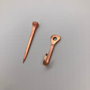 May include: Two copper-colored metal objects. One is a nail with a square head and the other is a hook with a round hole.