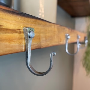 Pode incluir: Três ganchos de metal prateado são montados em uma prateleira de madeira. Os ganchos são curvos e têm um design simples.
