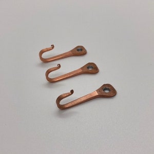May include: Three copper hooks with a simple design. Each hook has a rounded head with a small hole for hanging.