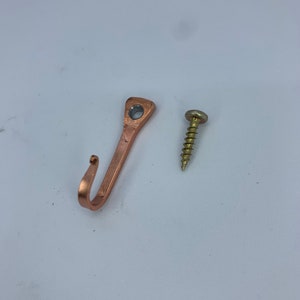 May include: A copper-colored hook with a screw for hanging items on a wall.