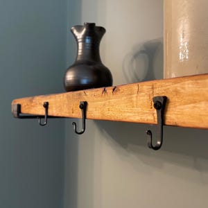 May include: A wooden shelf with four black metal hooks. A black ceramic jug sits on the shelf.