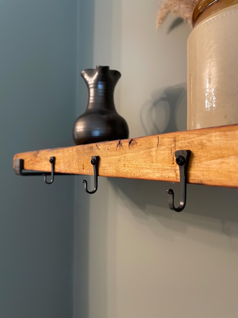 May include: A wooden shelf with four black metal hooks. A black ceramic jug sits on the shelf.