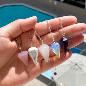 May include: Five crystal pendulum charms on silver chains. The charms are in the shapes of pyramids and are made of rose quartz, white howlite, clear quartz, opalite, and amethyst.