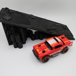 May include: A black 3D printed ramp with a textured surface and a red toy car with a white stripe and black wheels.