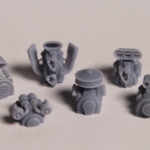 May include: Six different gray plastic model car engines. The engines are all different styles and sizes. Some have air filters, others have carburetors, and some have multiple exhaust pipes.