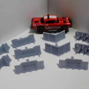 May include: A set of ten gray plastic barriers for a toy car race track. The barriers are in various shapes and sizes, including straight, curved, and angled pieces.