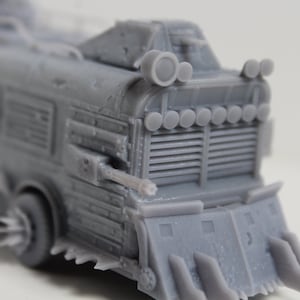 May include: A gray, detailed model of a heavily modified bus, featuring a front blade, multiple lights, and what appears to be a mounted weapon. The vehicle has a rugged, post-apocalyptic aesthetic, with visible vents and a textured surface.