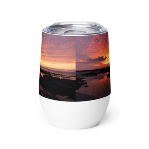 Può includere: Un bicchiere da vino in acciaio inossidabile bianco con un tramonto colorato sull'oceano riflesso nell'acqua. Il bicchiere ha un coperchio.