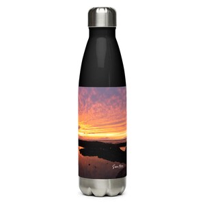 Può includere: Una bottiglia d'acqua in acciaio inossidabile con un tappo nero e un'immagine di tramonto colorato sul lato. L'immagine mostra un riflesso del tramonto nell'acqua.