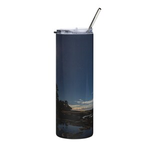 Può includere: Un bicchiere in acciaio inossidabile con un design blu scuro e nero che presenta un cielo notturno con stelle e un riflesso del cielo nell'acqua. Il bicchiere ha un coperchio trasparente e una cannuccia in acciaio inossidabile.