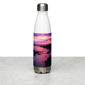 Può includere: Una bottiglia d'acqua in acciaio inossidabile bianca con una scena di tramonto colorata stampata sul lato. La scena presenta un cielo rosa e viola sopra una costa rocciosa con l'acqua che riflette i colori del cielo.