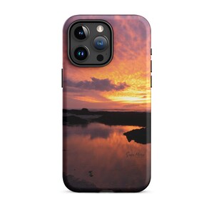 Può includere: Una custodia per telefono con un tramonto sul mare che si riflette nell'acqua. Il cielo è un mix di arancione, rosa e viola. La custodia ha un rigonfiamento della fotocamera nero con tre obiettivi.