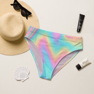 May include: A rainbow-colored swimsuit bottom with a high-waisted cut. The swimsuit is on a white background with a straw hat, sunglasses, and sunscreen.