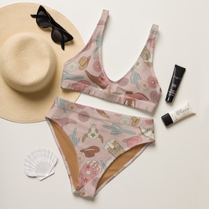 May include: A pink and brown bikini with a western print featuring cowboy boots, hats, and cacti. The bikini top has a scoop neck and adjustable straps. The bikini bottom has a high waist and full coverage.