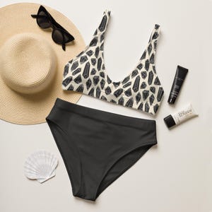 May include: A black and white patterned bikini top with a black high-waisted bikini bottom. The bikini top has a scoop neck and adjustable straps. The bikini bottom has a high-cut leg.