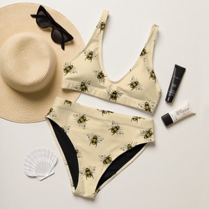 May include: A beige bikini with a black lining. The bikini top and bottom feature a repeating pattern of yellow and black bees.