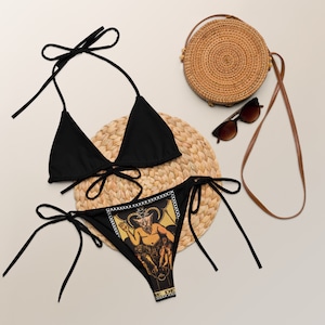 May include: Black bikini with a tarot card design featuring a devil figure. The bikini top is a triangle style with adjustable straps. The bottom is a cheeky style with adjustable ties on the sides.