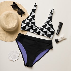 May include: Black and white shark tooth print bikini top and black bikini bottoms with a purple lining. A straw hat, sunglasses, sunscreen, and a seashell are also pictured.