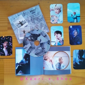 May include: A photocard set featuring a K-pop idol. The set includes a CD, a photobook, and several photocards. The photocards feature the idol in various poses and settings. The CD is a blue and white color with a collage of images. The photobook is a blue color with a photo of the idol on the cover. The photocards are all different colors and feature the idol in different outfits. The set is packaged in a clear plastic sleeve. The text on the CD says "TRACKLIST: 1. Promise - (Short Version) Live Version 2. 24/7 Heaven - Jimin & Taehyung 3. Graduation - Jimin & Taehyung 4. We won't talk anymore (Cover) - Jungkook & Taehyung 5. As told U - Jungkook & Taehyung Live Version"