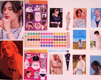 Puede incluir: Una colección de tarjetas de fotos con un joven de pelo largo. Las tarjetas están dispuestas sobre una superficie blanca con pegatinas y otros elementos decorativos. Las pegatinas presentan una variedad de diseños, incluyendo un oso, un corazón y letras del alfabeto. El texto "@kaori.s_shop" está escrito en la superficie.