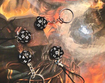 May include: Four black dice with white numbers on them are attached to keychains. The keychains are hanging from a book with the title "Tasha's Cauldron of Everything" on the cover.